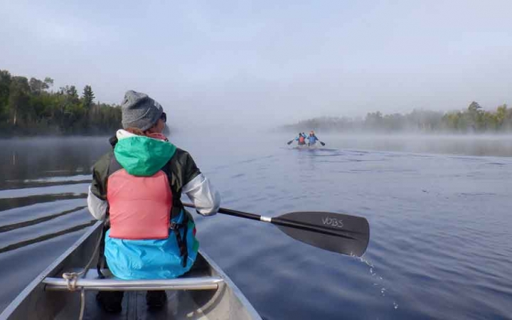 a student in a canoe paddles on calm water into the fog 